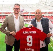 Andreas Weber (Geschäftsführer Rudolf Weber) und Fernando Carro de Prada (Vorsitzender Geschäftsführer Bayer Leverkusen) halten in der BayArena ein Trikot von Bayer Leverkusen in die Kamera.