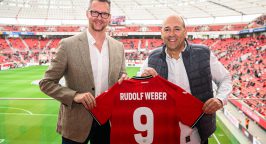 Andreas Weber (Geschäftsführer Rudolf Weber) und Fernando Carro de Prada (Vorsitzender Geschäftsführer Bayer Leverkusen) halten in der BayArena ein Trikot von Bayer Leverkusen in die Kamera.