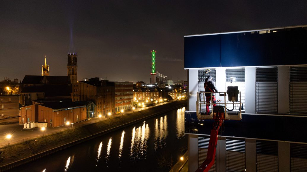 EIn Mitarbeiter von Rudolf Weber steht auf einem Hubsteiger und reinigt Fenster im Duisburger Innenhafen. Im Hintergrund ist der Turm der Stadtwerke zu sehen.