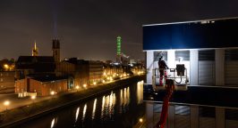 EIn Mitarbeiter von Rudolf Weber steht auf einem Hubsteiger und reinigt Fenster im Duisburger Innenhafen. Im Hintergrund ist der Turm der Stadtwerke zu sehen.