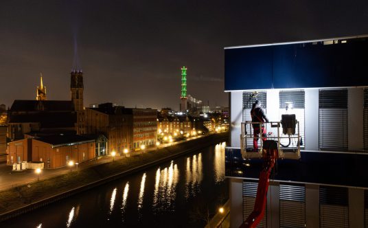 EIn Mitarbeiter von Rudolf Weber steht auf einem Hubsteiger und reinigt Fenster im Duisburger Innenhafen. Im Hintergrund ist der Turm der Stadtwerke zu sehen.