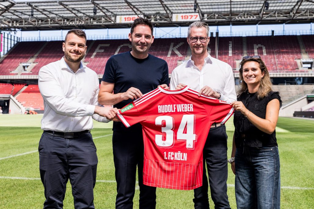 Stephan Rathgeber, Florian Dederichs, Andreas Weber und Lara Friese halten ein Trikot mit der Nummer 34 und dem Namen "Rudolf Weber" in die Kamera.