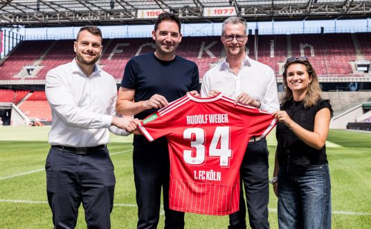 Stephan Rathgeber, Florian Dederichs, Andreas Weber und Lara Friese halten ein Trikot mit der Nummer 34 und dem Namen "Rudolf Weber" in die Kamera.